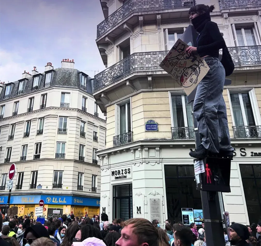 Une manifestante perchée sur un feu tricolore au-dessus de la foule, pancarte à la main, boulevard Voltaire à Paris