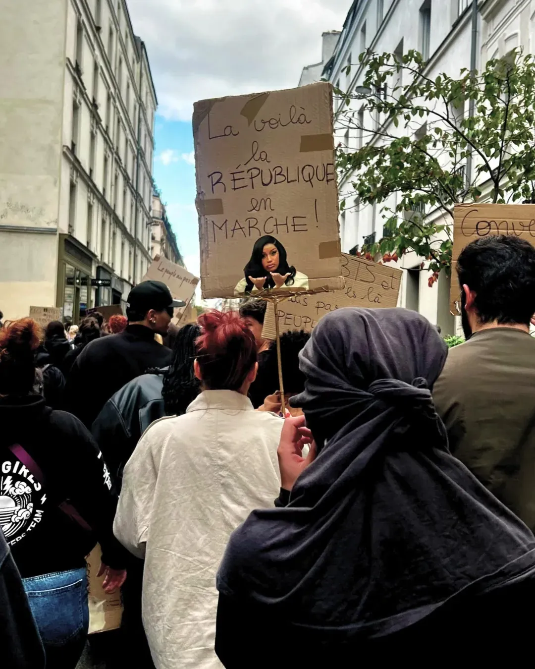 Pancarte en carton « La voilà la République en marche ! » brandie au-dessus d’une foule dans une rue étroite de Paris
