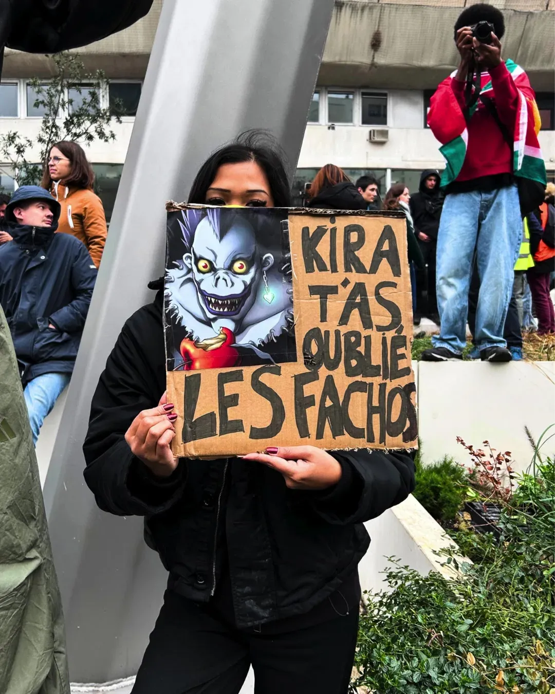 Une manifestante tient une pancarte avec le dieu de la mort Ryuk du manga Death Note et le texte « Kira, t’as oublié les fachos »