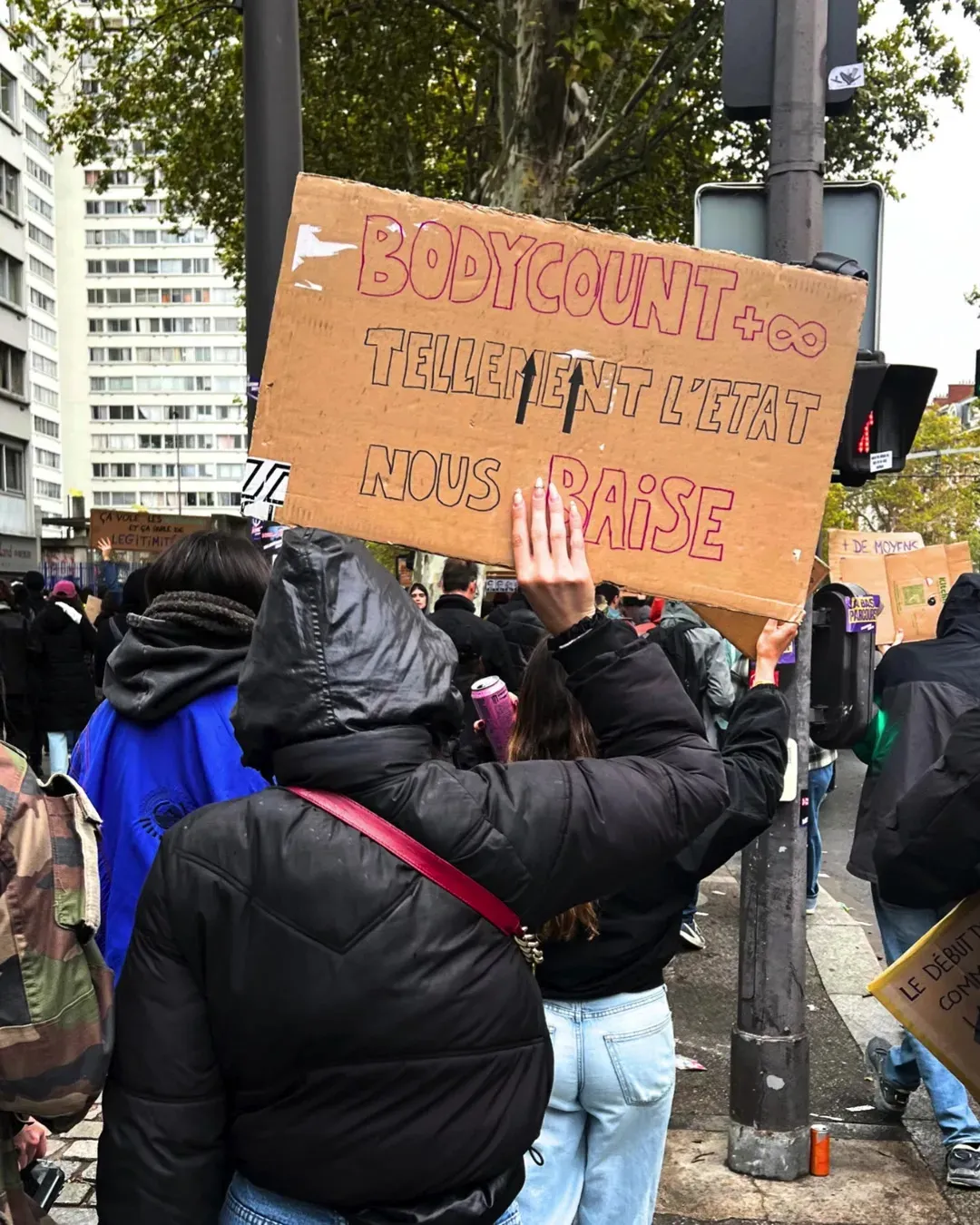 Une manifestante de dos, capuche noire, brandit une pancarte « Bodycount + infini, tellement l’État nous baise »