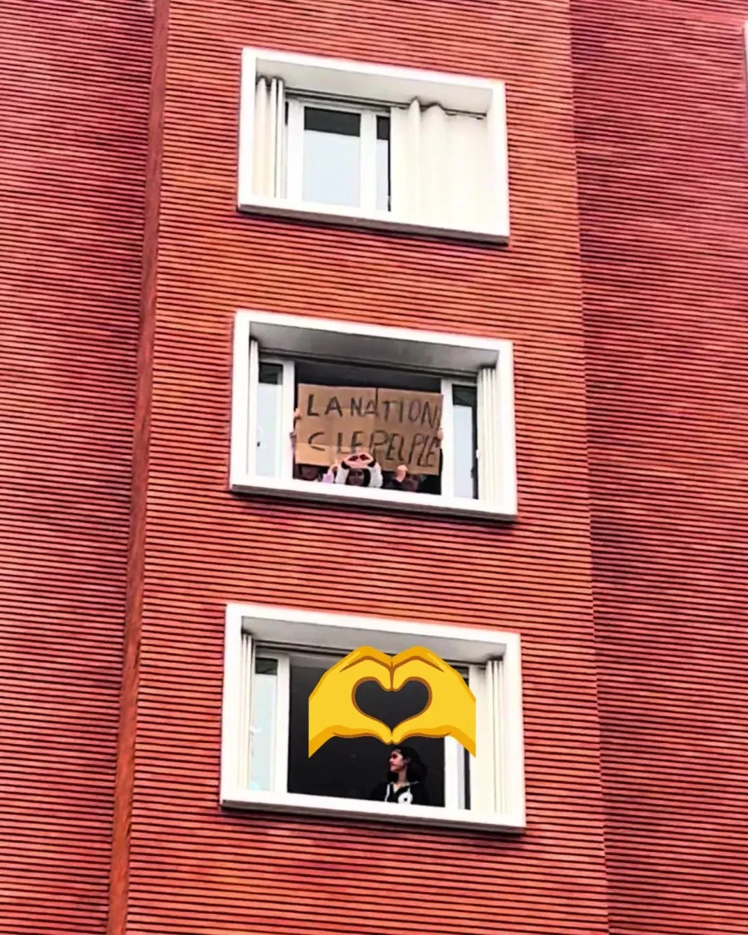 Une façade de briques rouges, une pancarte « La Nation c’est le peuple » tendue à une fenêtre et, deux étages plus bas, une femme qui regarde le cortège