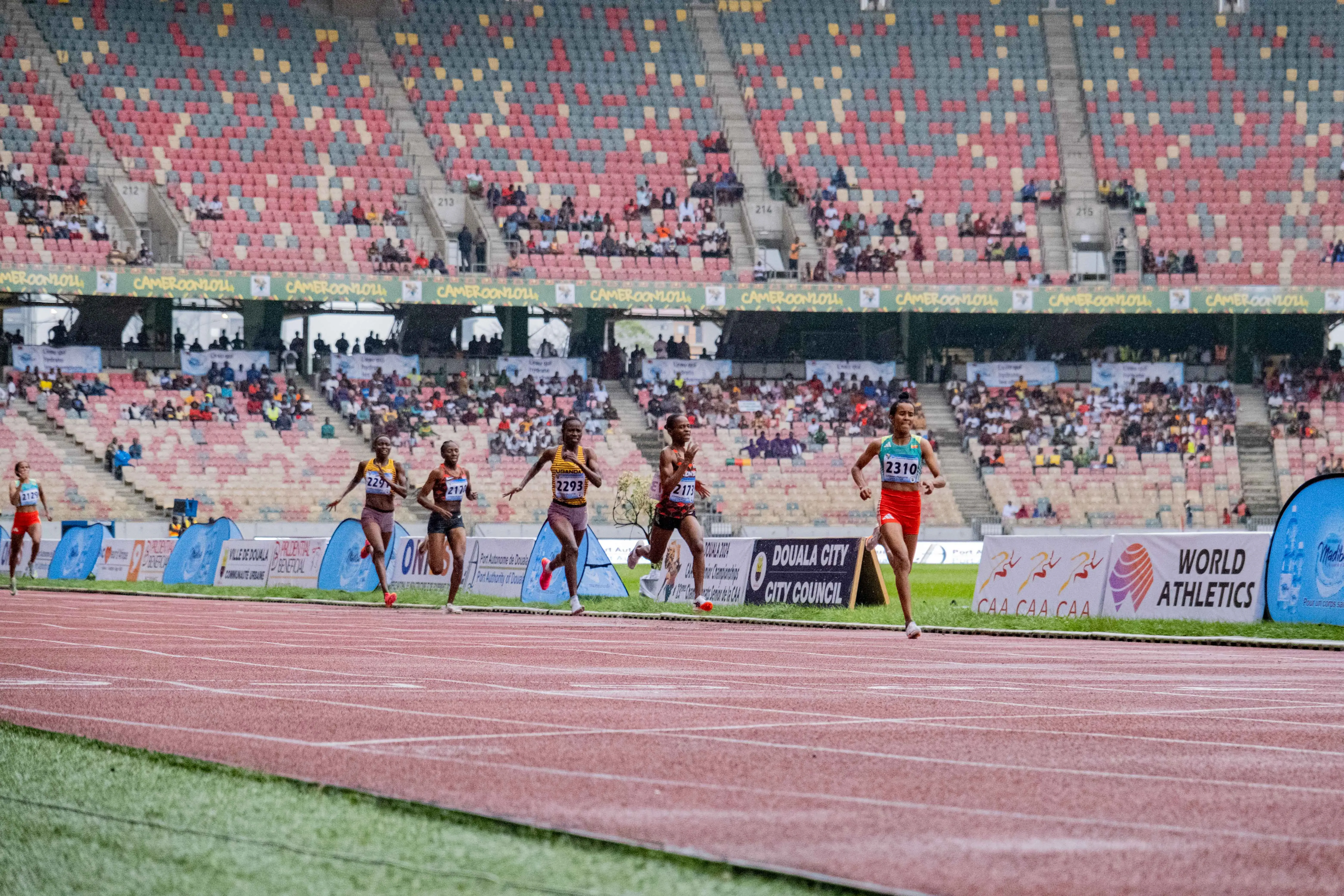 Un groupe d’athlètes féminines sprintent sur une piste d’athlétisme lors d’une finale de 1500 mètres, dans un stade au public clairsemé