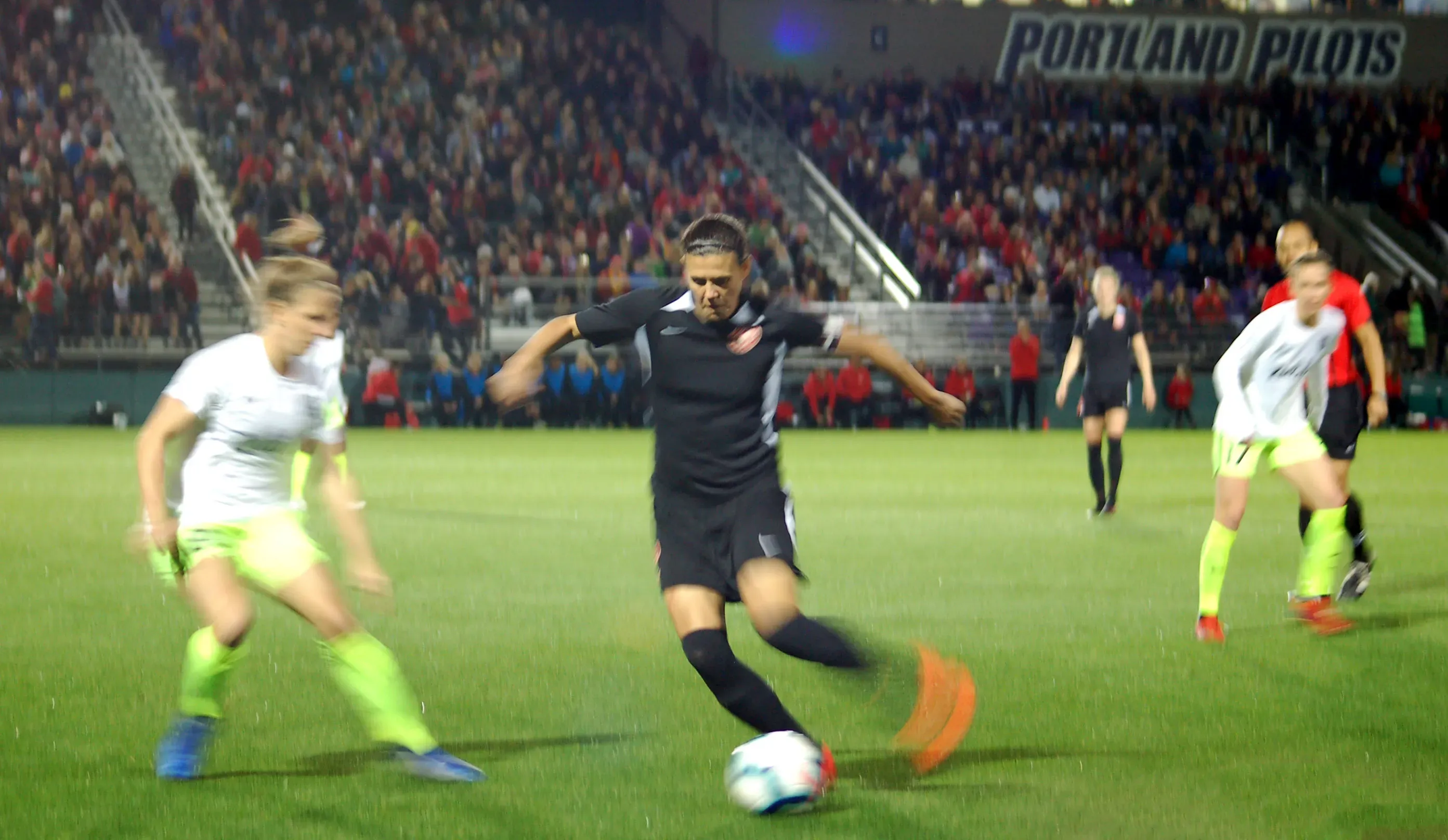 Christine Sinclair, en maillot noir, frappe le ballon lors d’un match de soccer disputé sous la pluie devant un stade plein