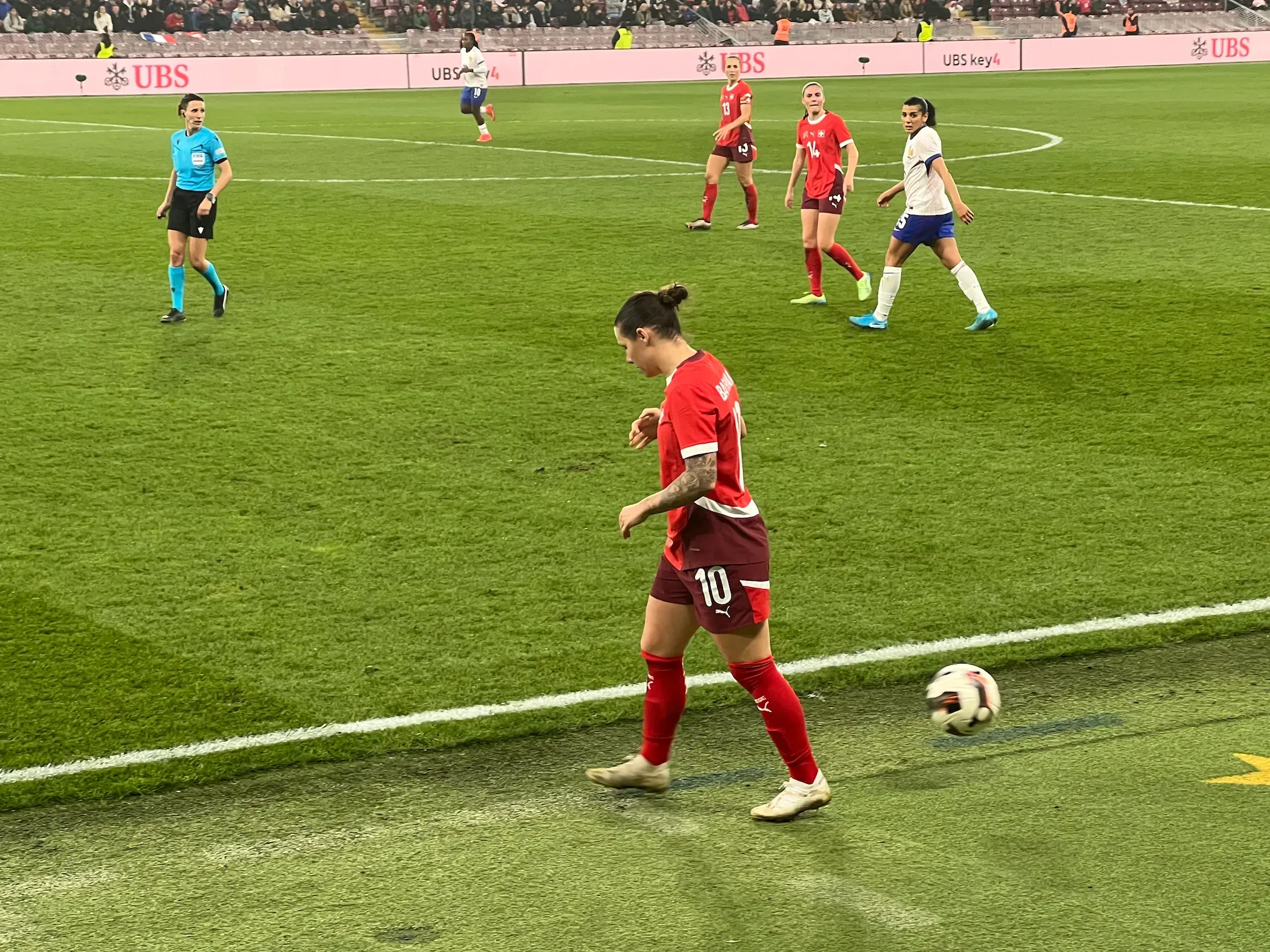 Une joueuse de l’équipe de Suisse contrôle le ballon devant une joueuse de l’équipe de France lors d’un match international féminin de football, stade aux tribunes clairsemées
