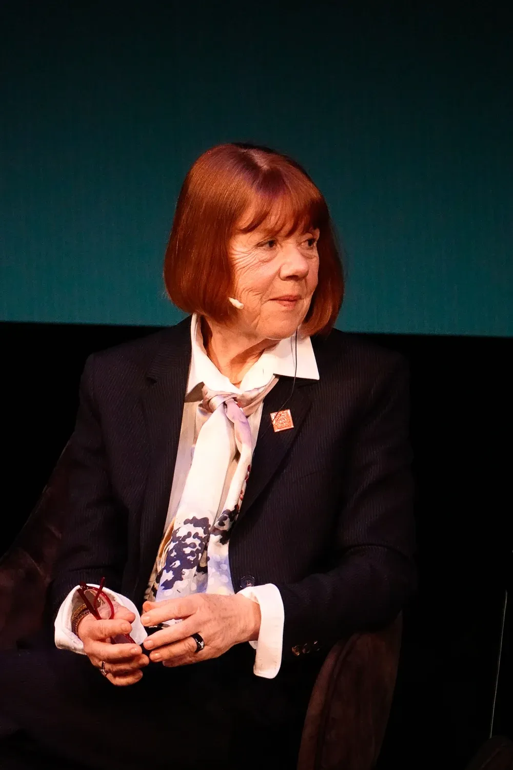 Portrait de Gisèle Pelicot, cheveux roux mi-longs, assise, lors d’une rencontre publique