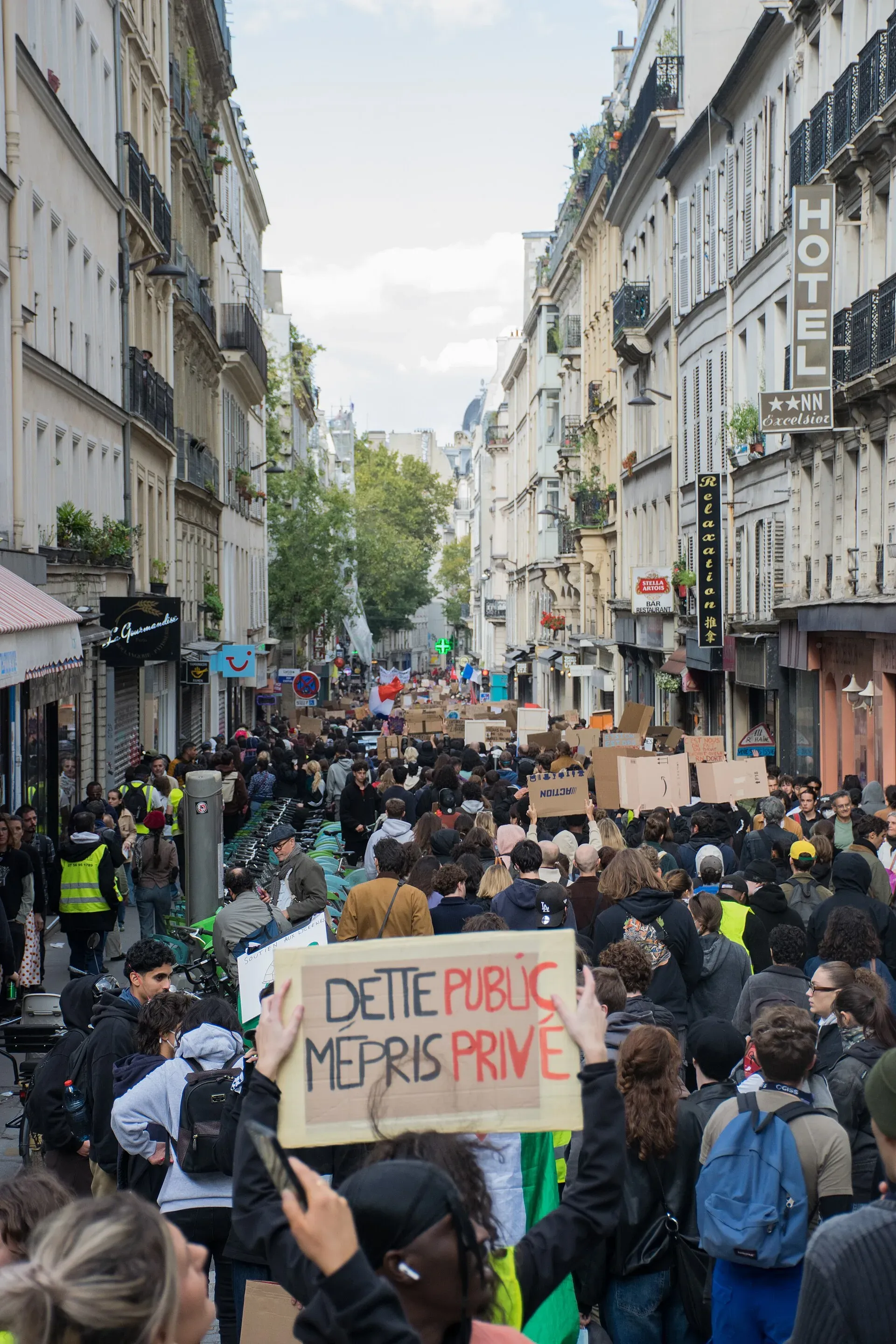 Cortège de la manifestation du 17 octobre 2026 à Paris, une pancarte en carton « Dette public, mépris privé » brandie au premier plan