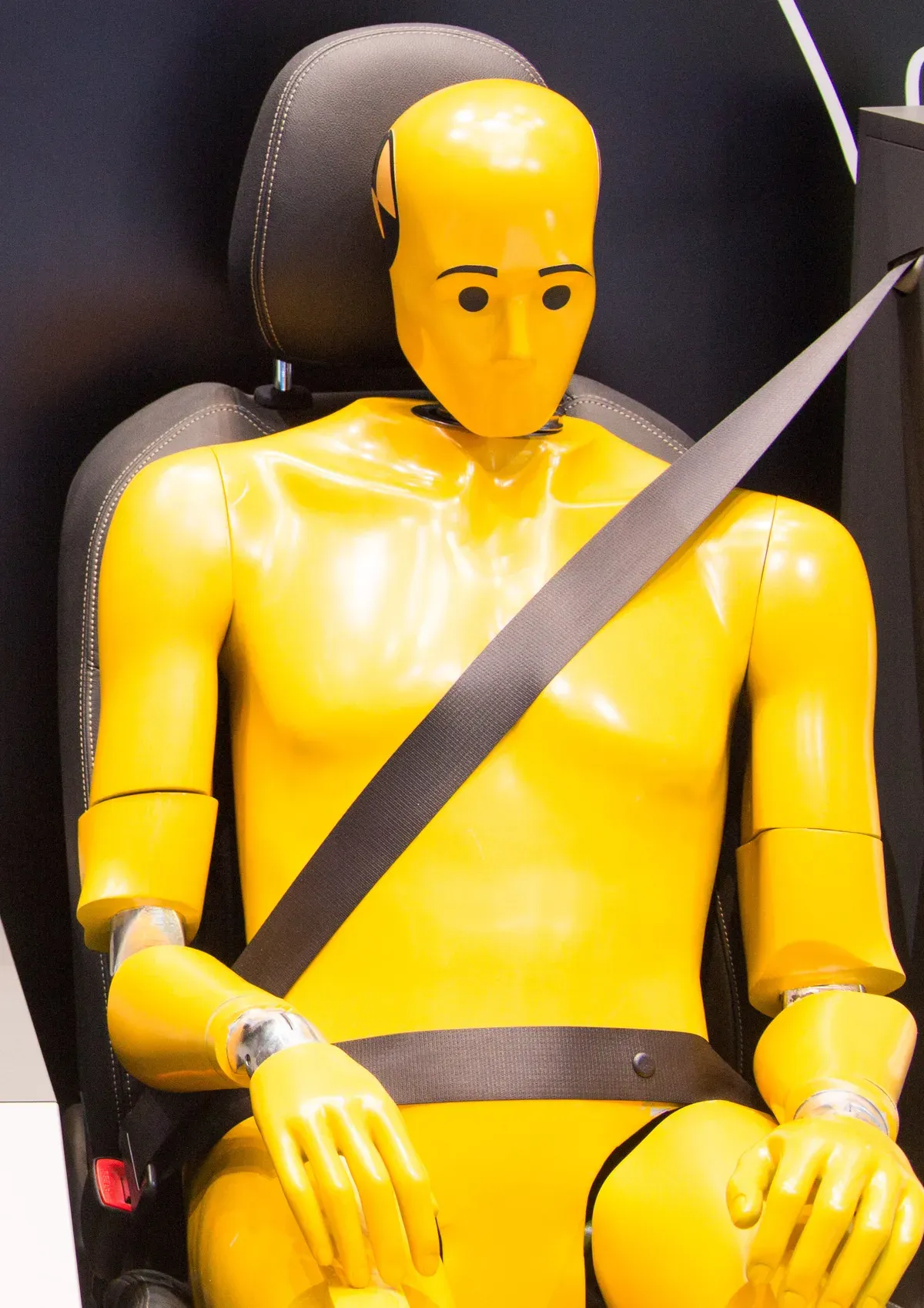 Mannequin de crash test jaune assis sur un siège auto, sanglé par une ceinture de sécurité trois points