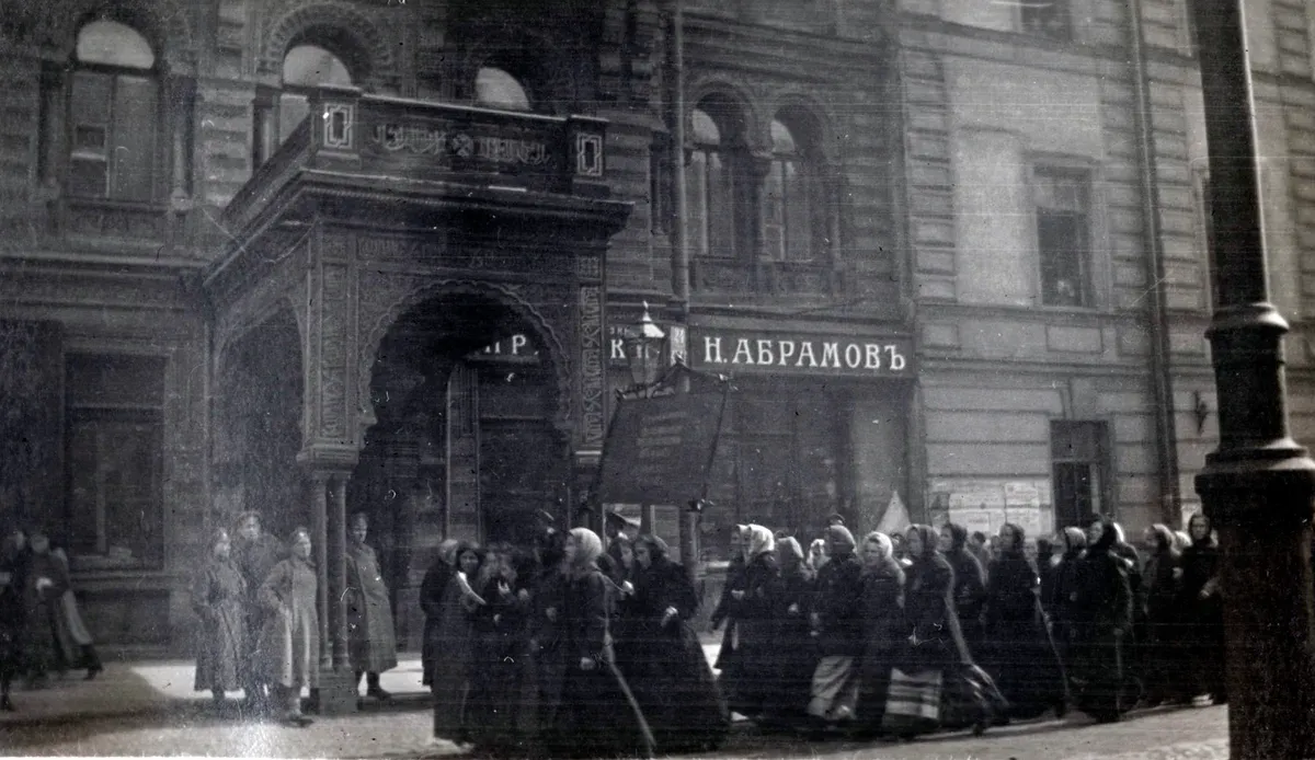 Cortège de femmes en fichus marchant dans une rue de Petrograd en 1917, devant la boutique N. Abramov, sous le regard de passants