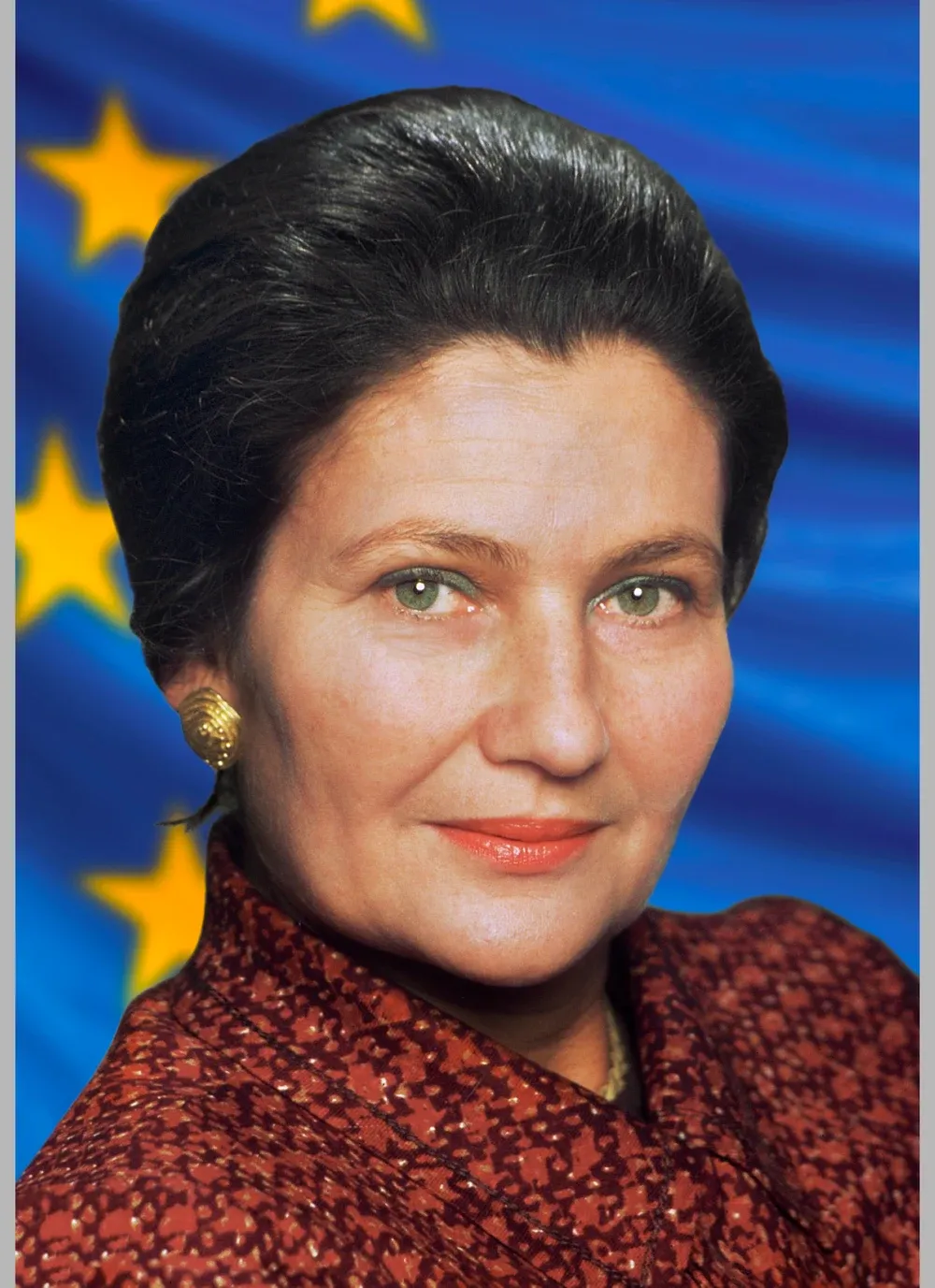 Portrait officiel de Simone Veil, cheveux courts, veste rouge, devant le drapeau européen