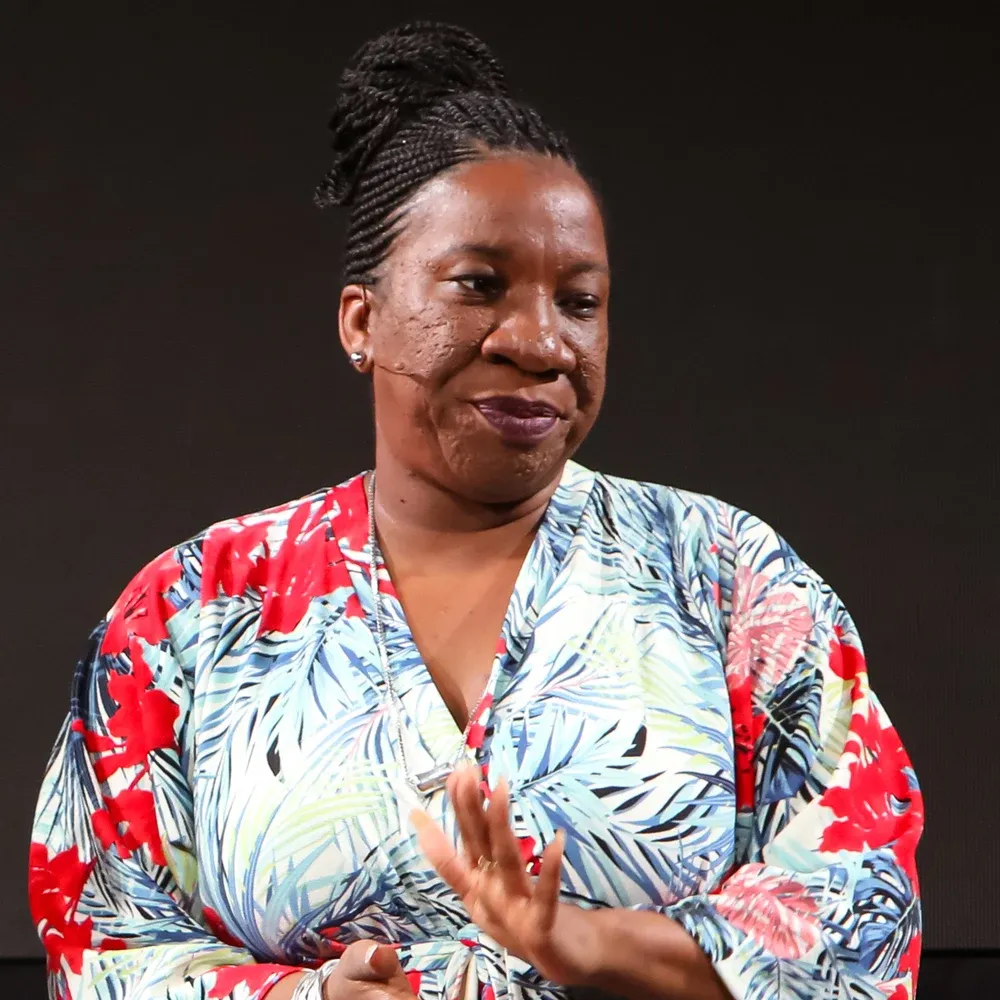 Portrait de Tarana Burke en gros plan, cheveux tressés relevés, souriante